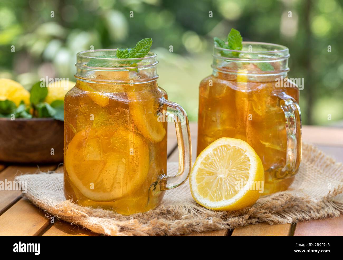 Thé glacé dans des pots en verre avec des tranches de citron et menthe dehors sur table en bois avec fond de nature Banque D'Images