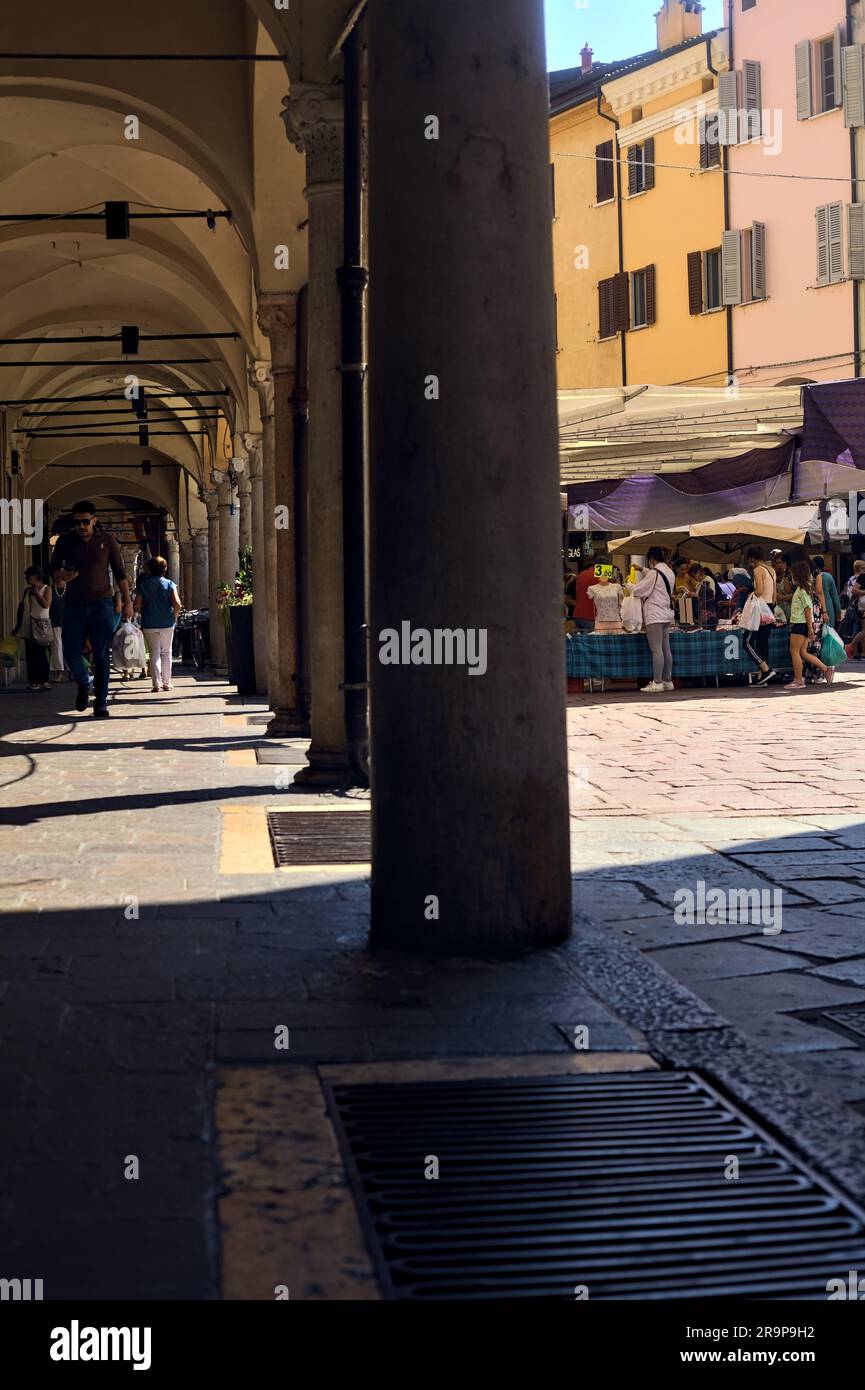 Place avec des stands et des personnes passant par un jour ensoleillé dans une ville italienne vue d'un porche à l'ombre Banque D'Images