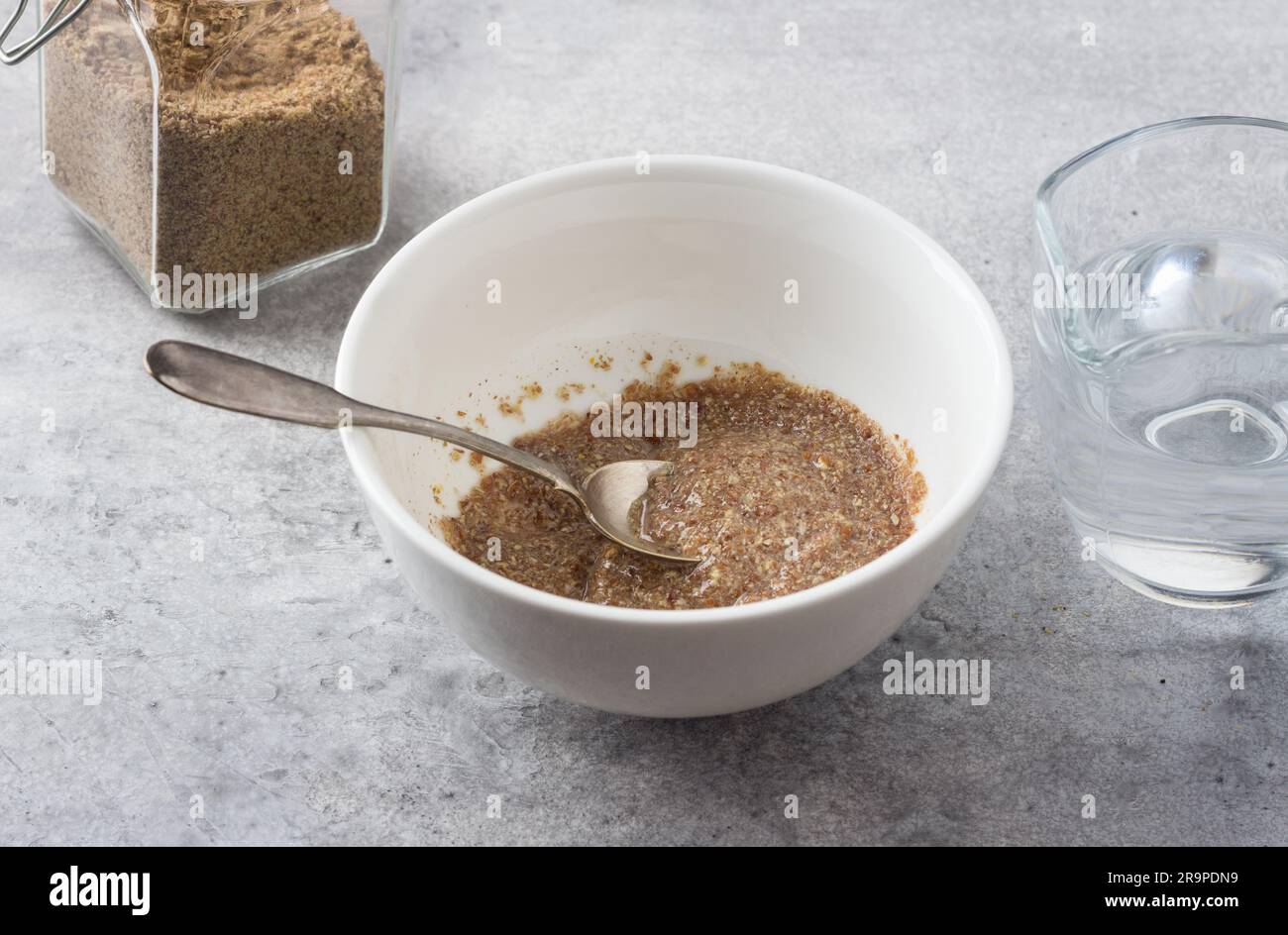 Un bol avec du lin moulu et de l'eau, un pot de lin moulu et un pot d'eau sur fond texturé gris. Cuisson d'un œuf de lin végétalien. Banque D'Images