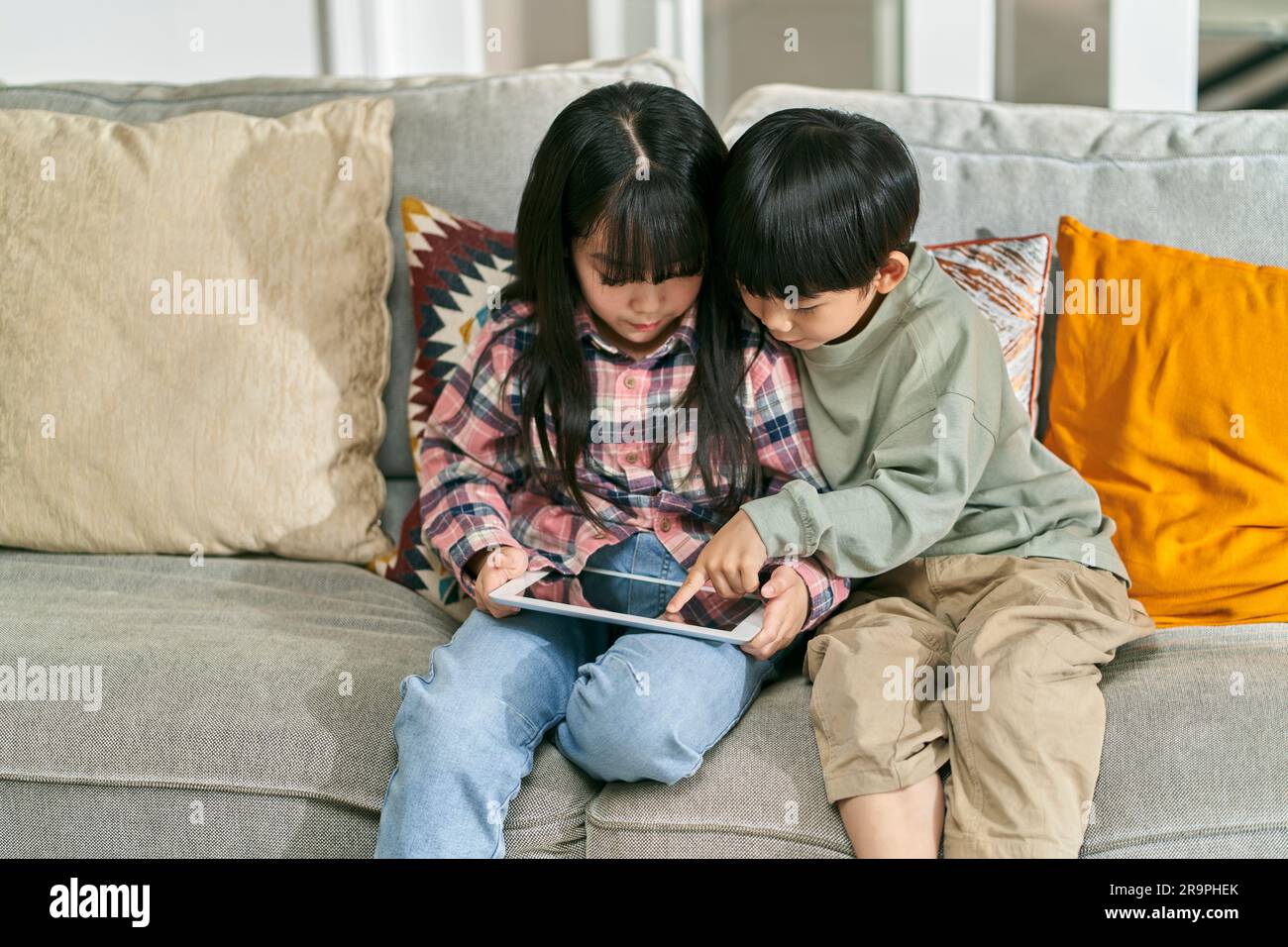 deux enfants asiatiques frère et soeur assis sur un canapé de famille à la maison jouant à un jeu d'ordinateur à l'aide d'une tablette numérique Banque D'Images