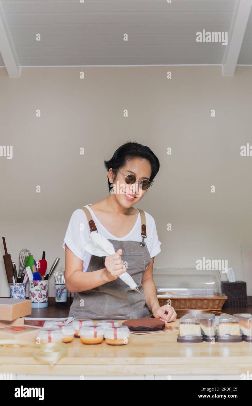 Une pâtisserie avec un sac de pâtisserie dans ses mains presse la crème sur un gâteau dans une salle de boulangerie. Banque D'Images