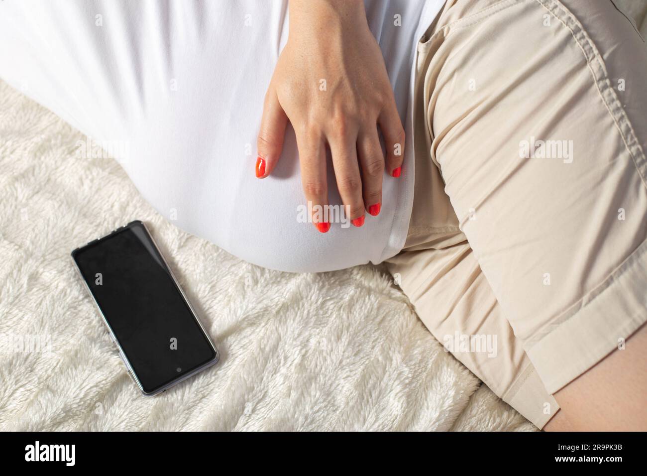 Une femme enceinte tient un téléphone portable près de son ventre. La  notion de préjudice et d'écarts dans le développement de l'enfant à naître.  L'impact négatif de Photo Stock - Alamy