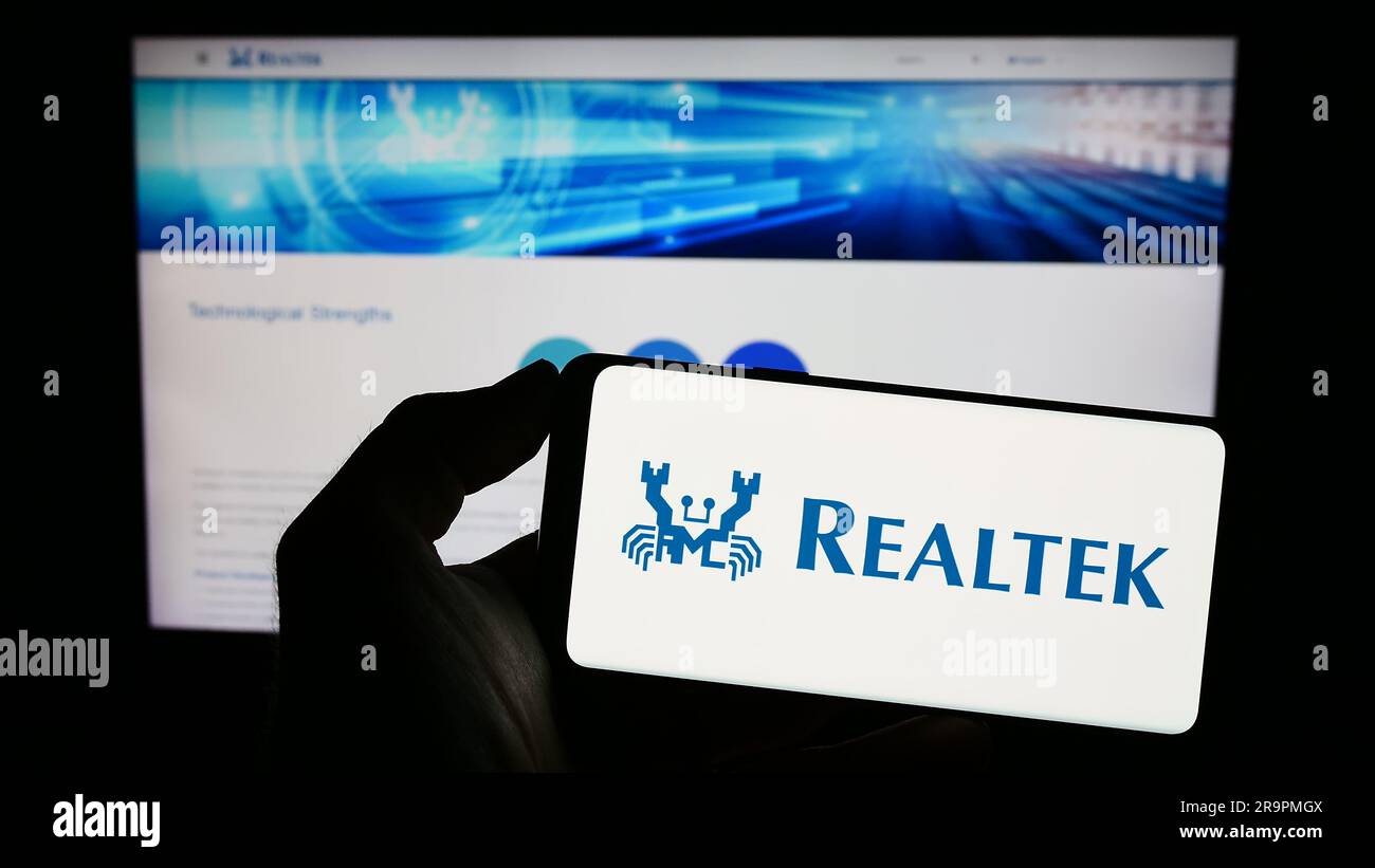 Personne tenant un téléphone portable avec le logo de la société taïwanaise Realtek Semiconductor Corp. à l'écran en face de la page Web. Mise au point sur l'affichage du téléphone. Banque D'Images