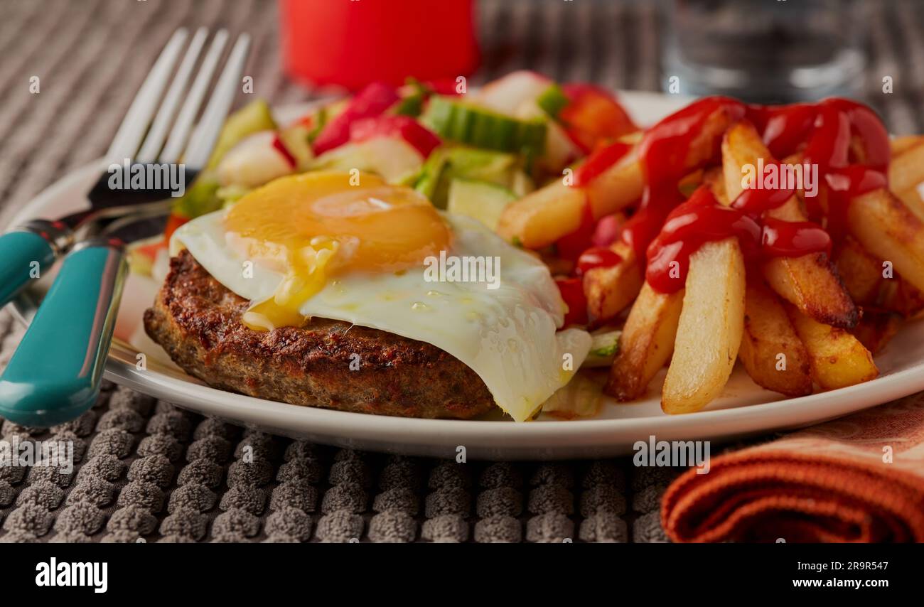 Déjeuner de pub avec frites, hamburger de bœuf recouvert d'œufs frits et de salade. Banque D'Images