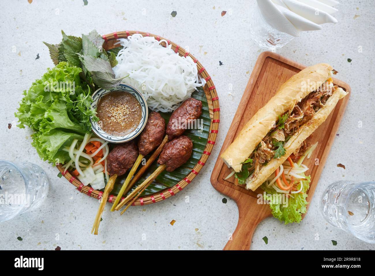 Goût du Vietnam. Cuisine vietnamienne traditionnelle sur table dans le restaurant. Boulettes de porc, nouilles, salade et sandwich Banh mi. Banque D'Images