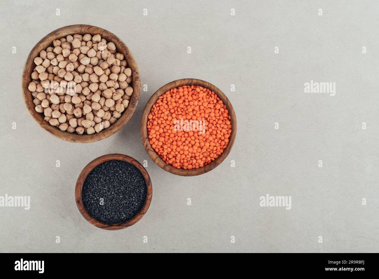 Lentilles rouges biologiques sèches, graines de sésame noir et pois chiches dans un bol en bois sur fond de béton. Vue de dessus Banque D'Images