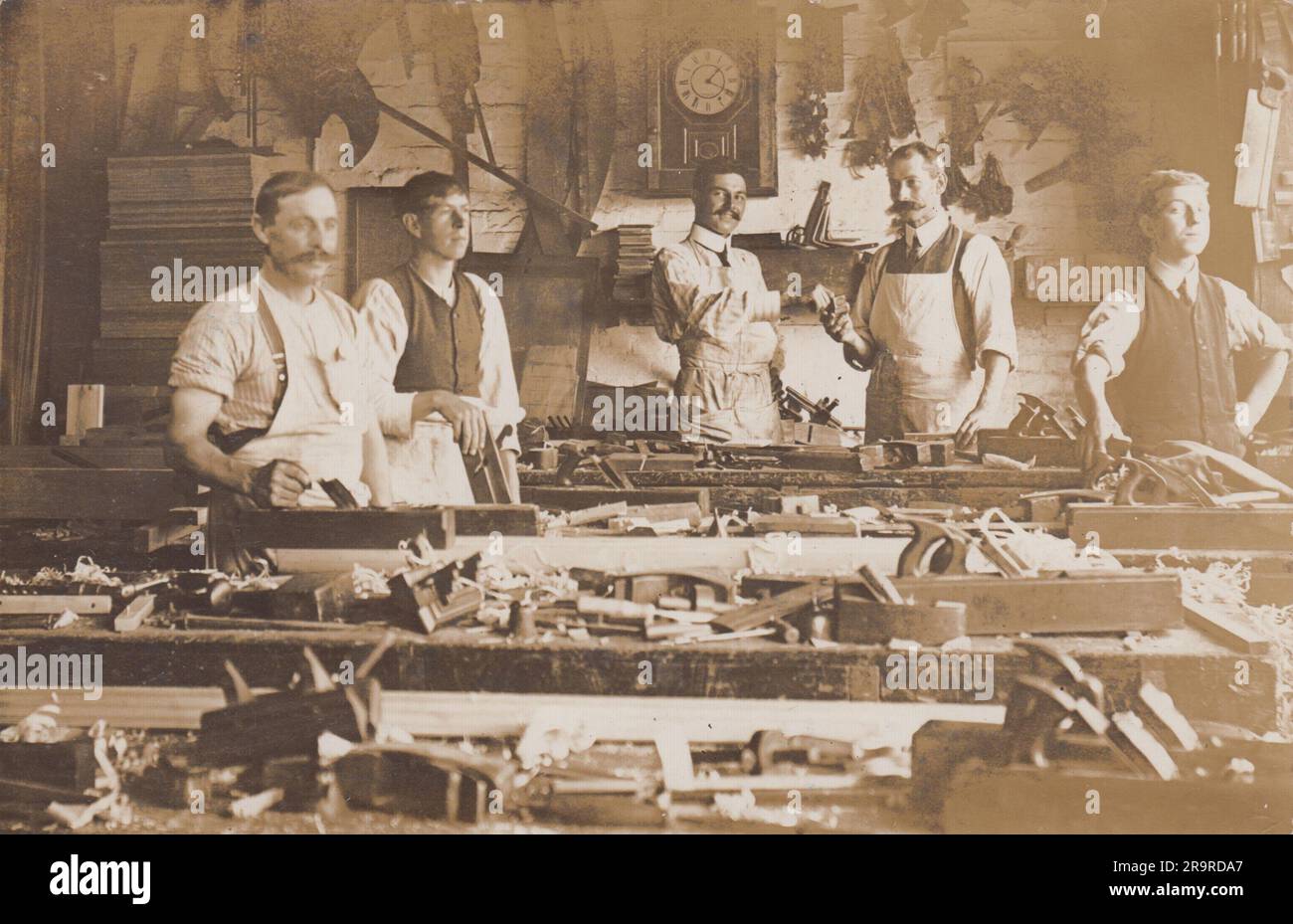 Atelier de charpentiers édouardiens, début du 20th siècle : photographie de cinq ouvriers debout derrière des bancs avec des outils de menuiserie empilés sur le dessus, plusieurs portent des tabliers Banque D'Images