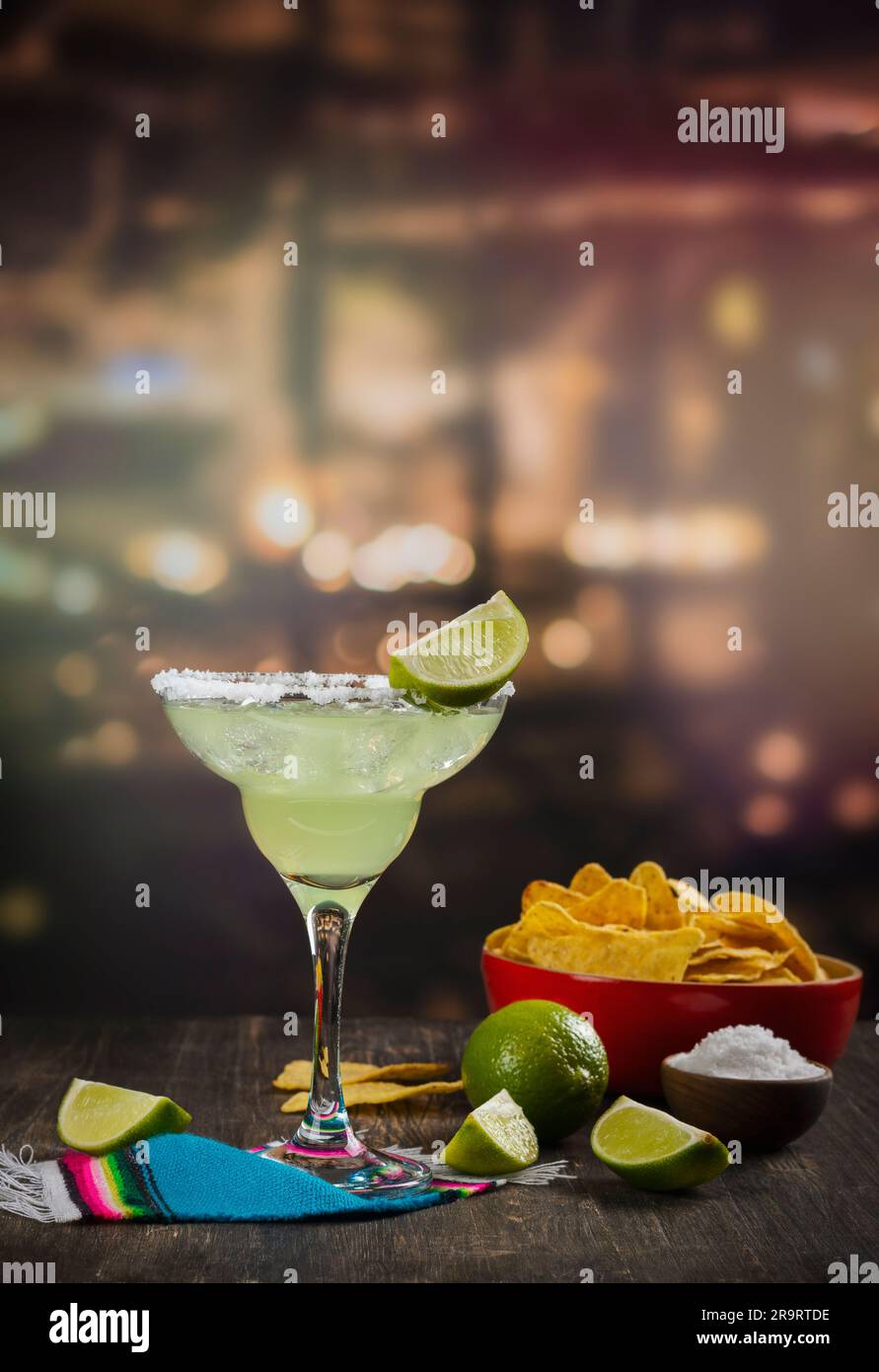 Cocktail de Margarita avec des limes entières et tranchées, nachos et sel sur une table de bar en bois. Ambiance de fête mexicaine Banque D'Images