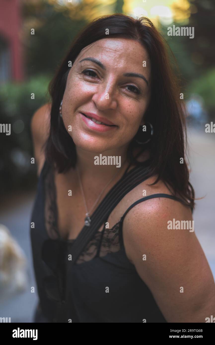 Portrait d'une femme brune vêtue d'une robe noire, penchée vers l'appareil photo en extérieur. Banque D'Images