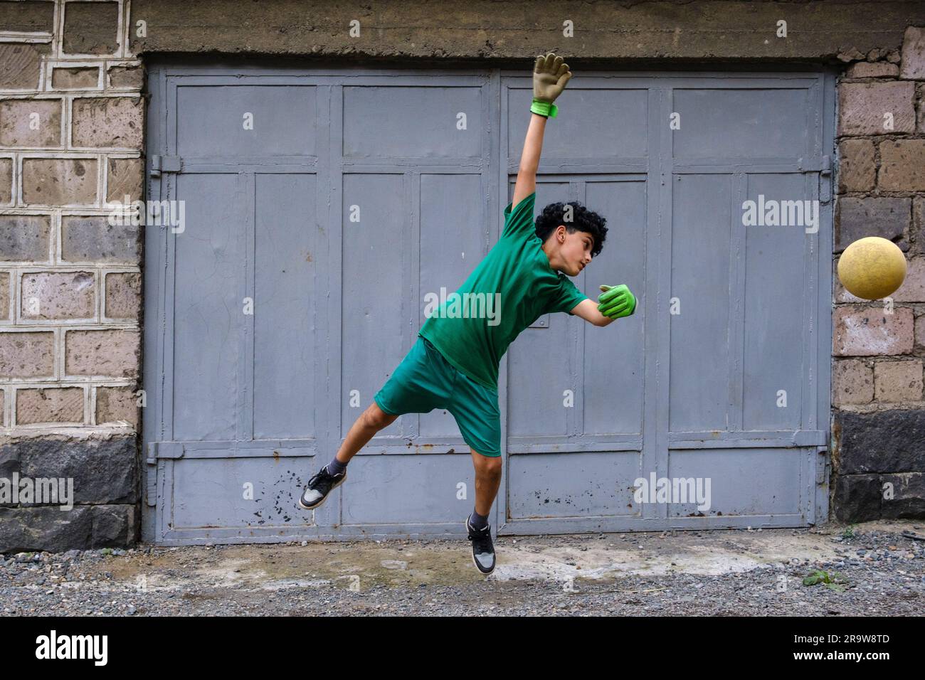 Un garçon avec le ballon comme gardien de but dans une cour arrière à Vagharshapat Banque D'Images