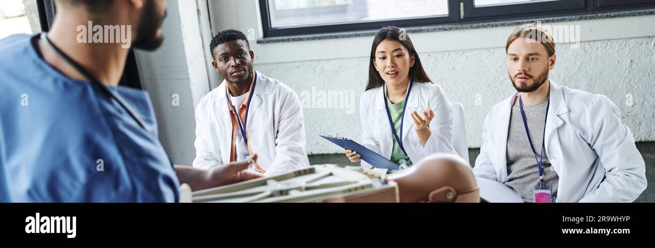Une jeune femme asiatique pose une question à un instructeur médical avec un mannequin de RCR lors d'un séminaire de premiers soins avec des étudiants interraciaux, acquérant et pratiquant Banque D'Images