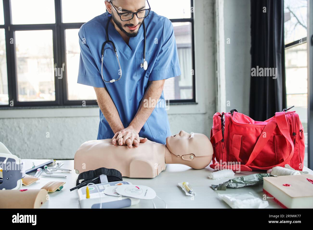 Jeunes professionnels paramédicaux pratiquant des compressions thoraciques sur un mannequin de RCP près d'un sac de premiers soins rouge, d'un défibrillateur automatisé et d'appareils médicaux en train Banque D'Images