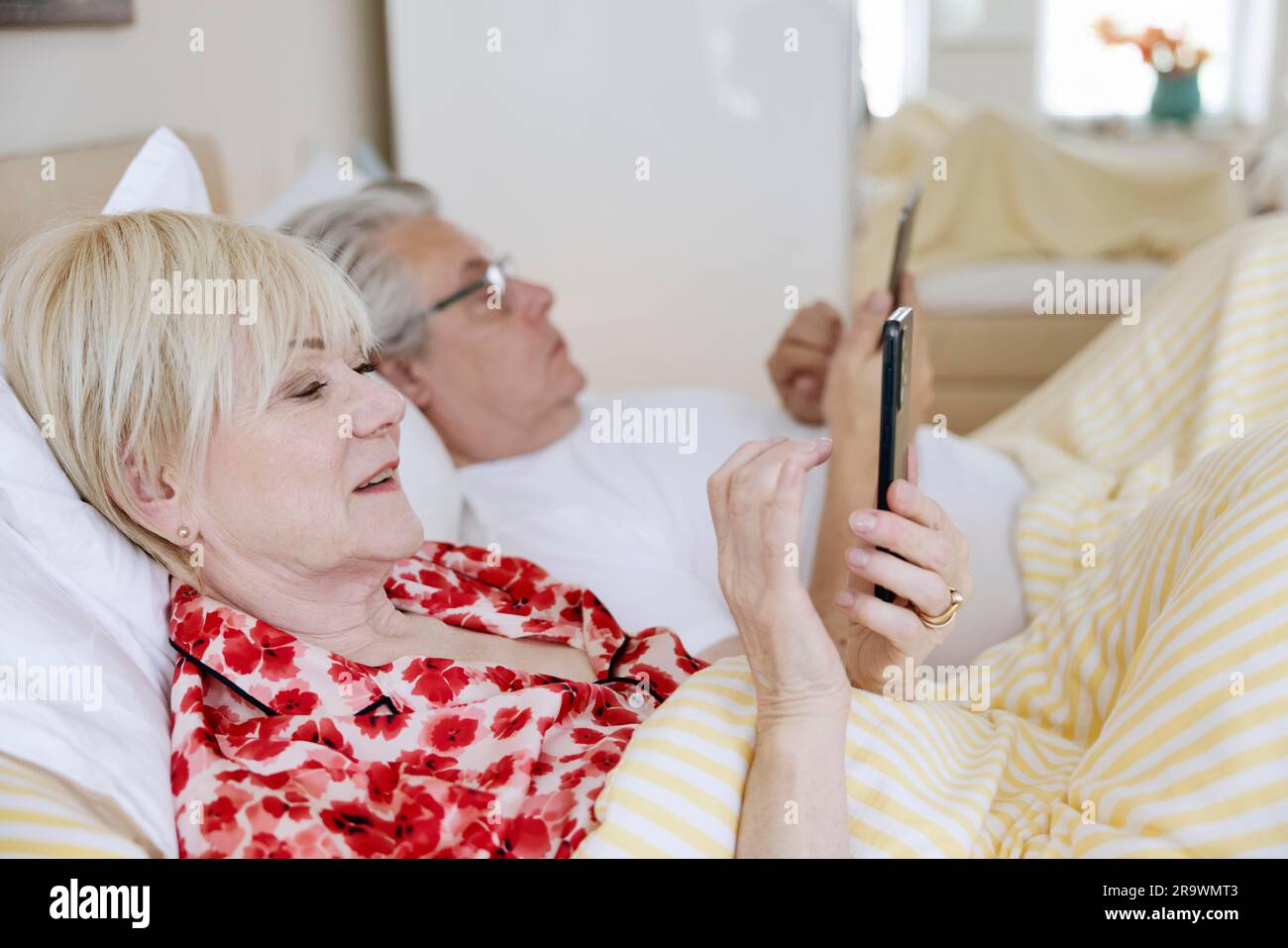 Couple âgé allongé dans un lit dans leur chambre, chacun regardant son propre smartphone, Cologne, Rhénanie-du-Nord-Westphalie, Allemagne Banque D'Images