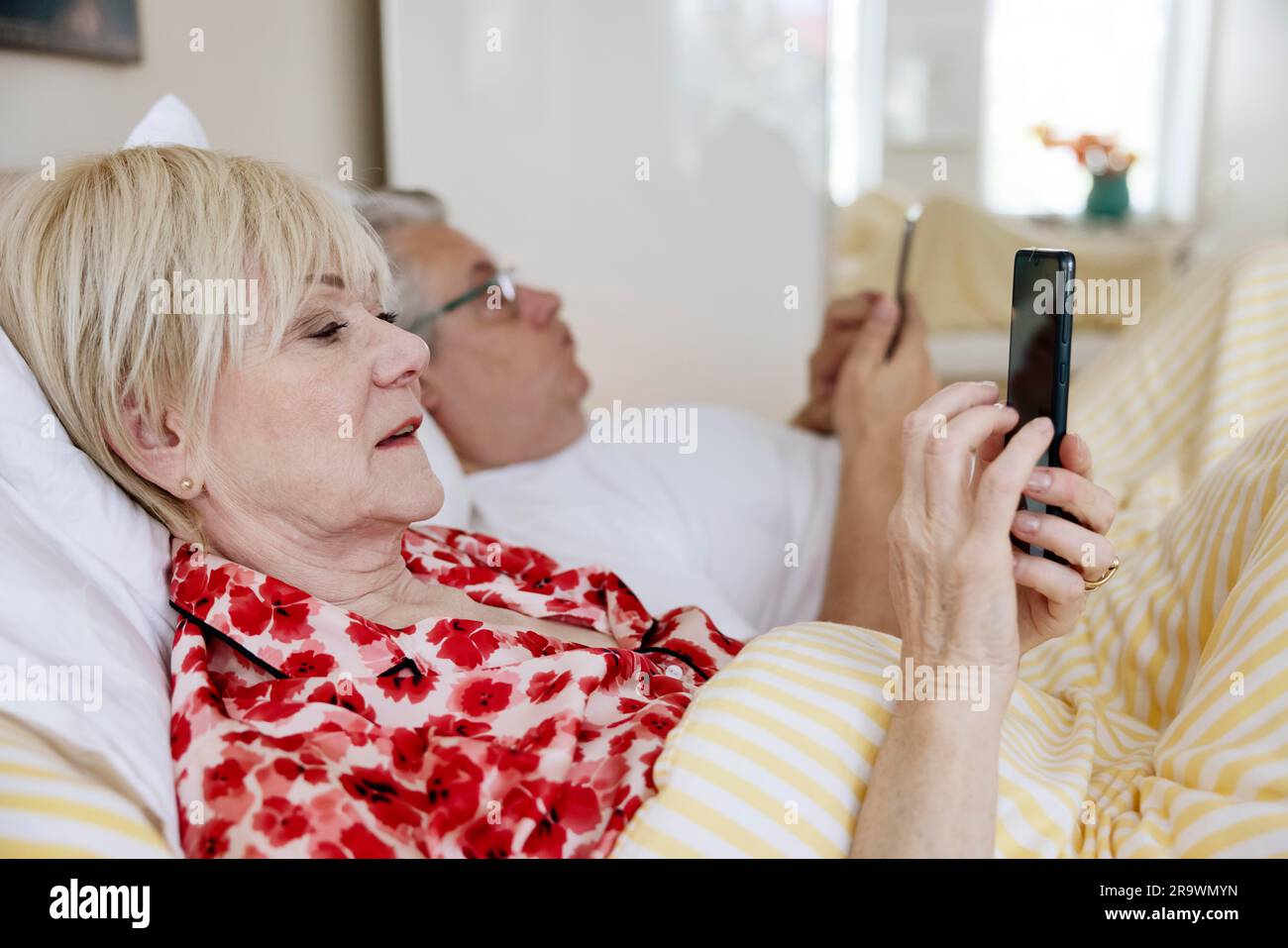 Couple âgé allongé dans un lit dans leur chambre, chacun regardant son propre smartphone, Cologne, Rhénanie-du-Nord-Westphalie, Allemagne Banque D'Images