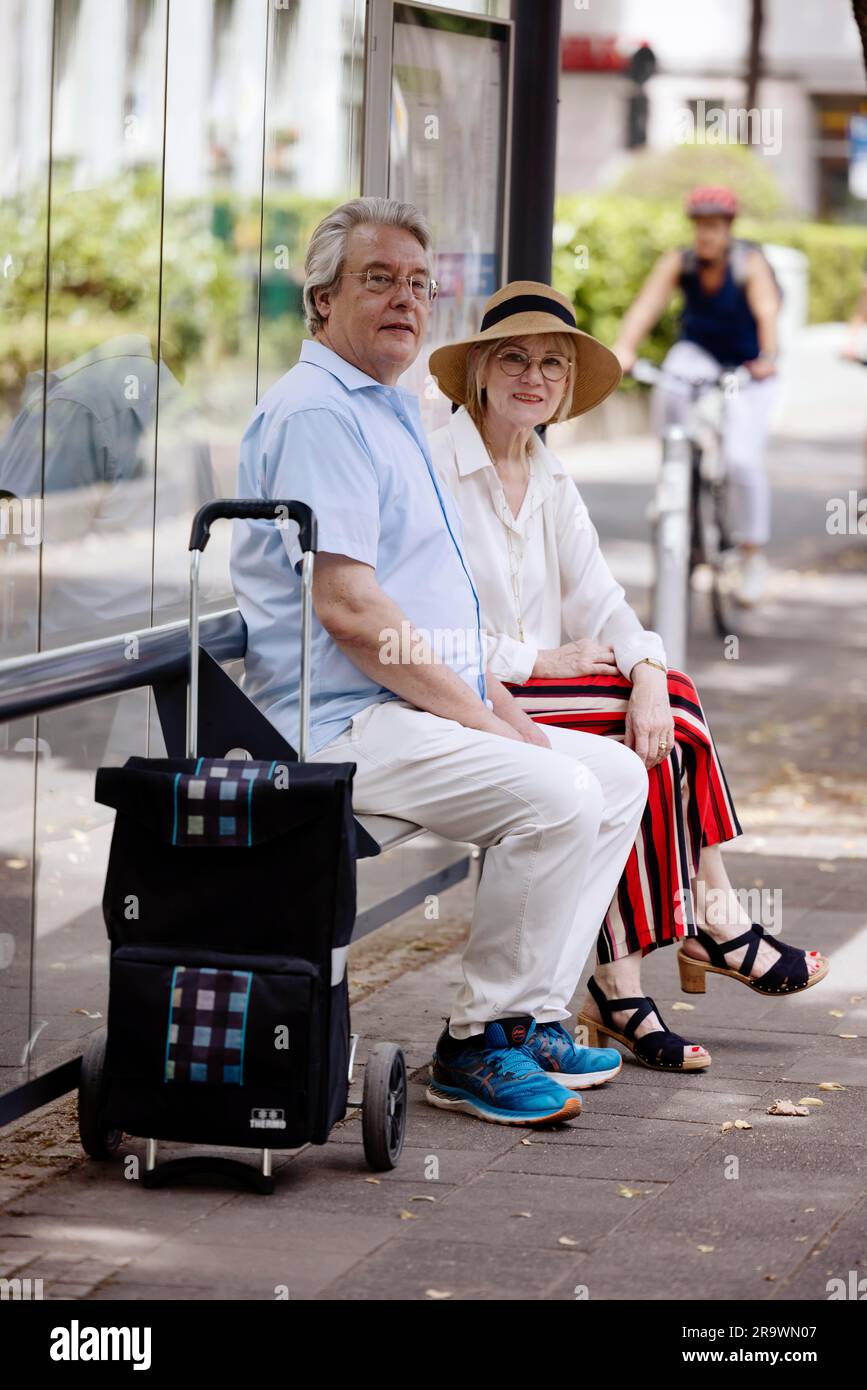 Un couple plus âgé vêtu de vêtements d'été avec un chariot attendant un bus à un arrêt de bus, Cologne, Rhénanie-du-Nord-Westphalie, Allemagne Banque D'Images