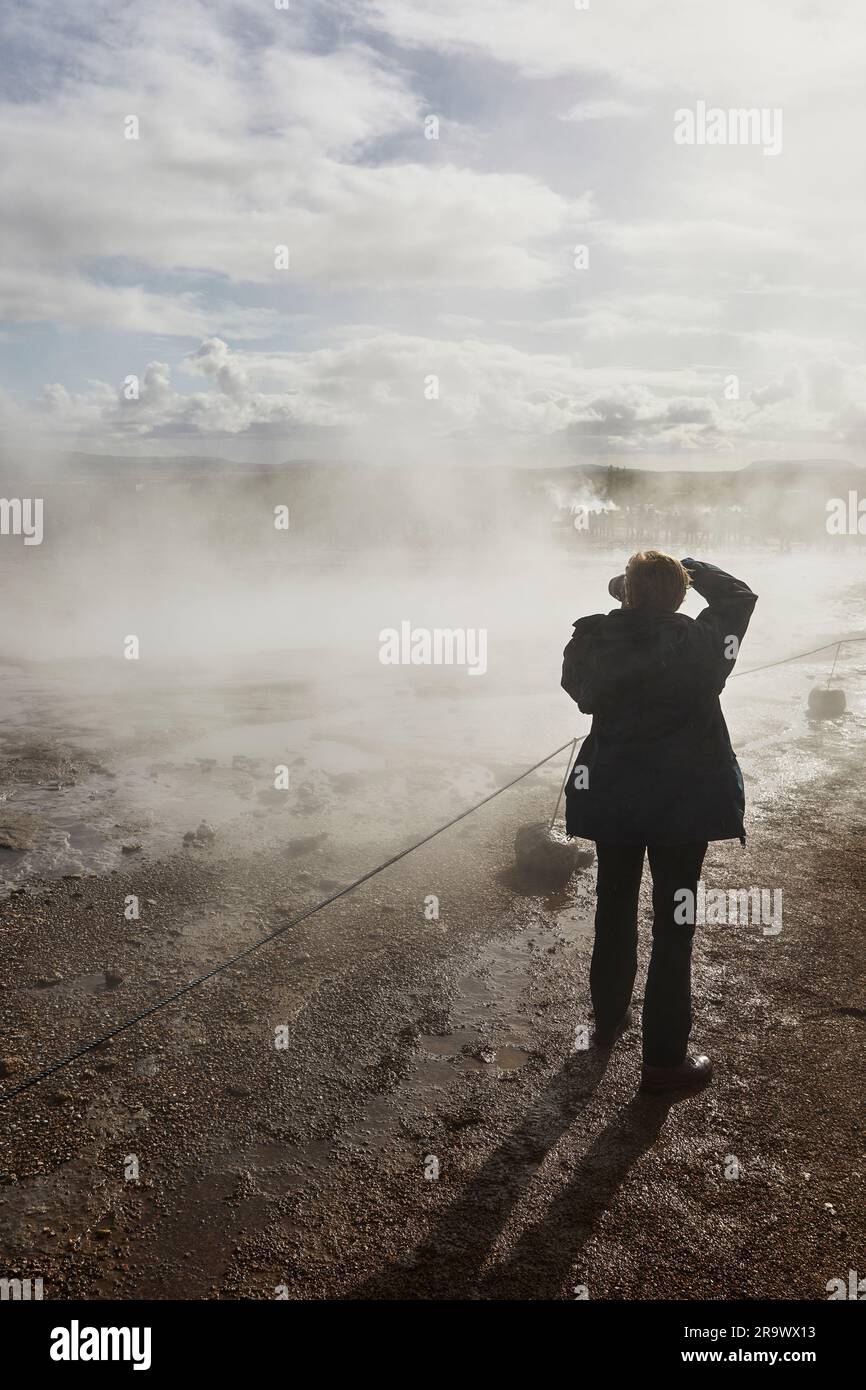 Un photographe photographiant dans la lumière du soleil et les embruns de Strokkur Geysir, à Geysir, dans le cercle d'Or, Islande. Banque D'Images