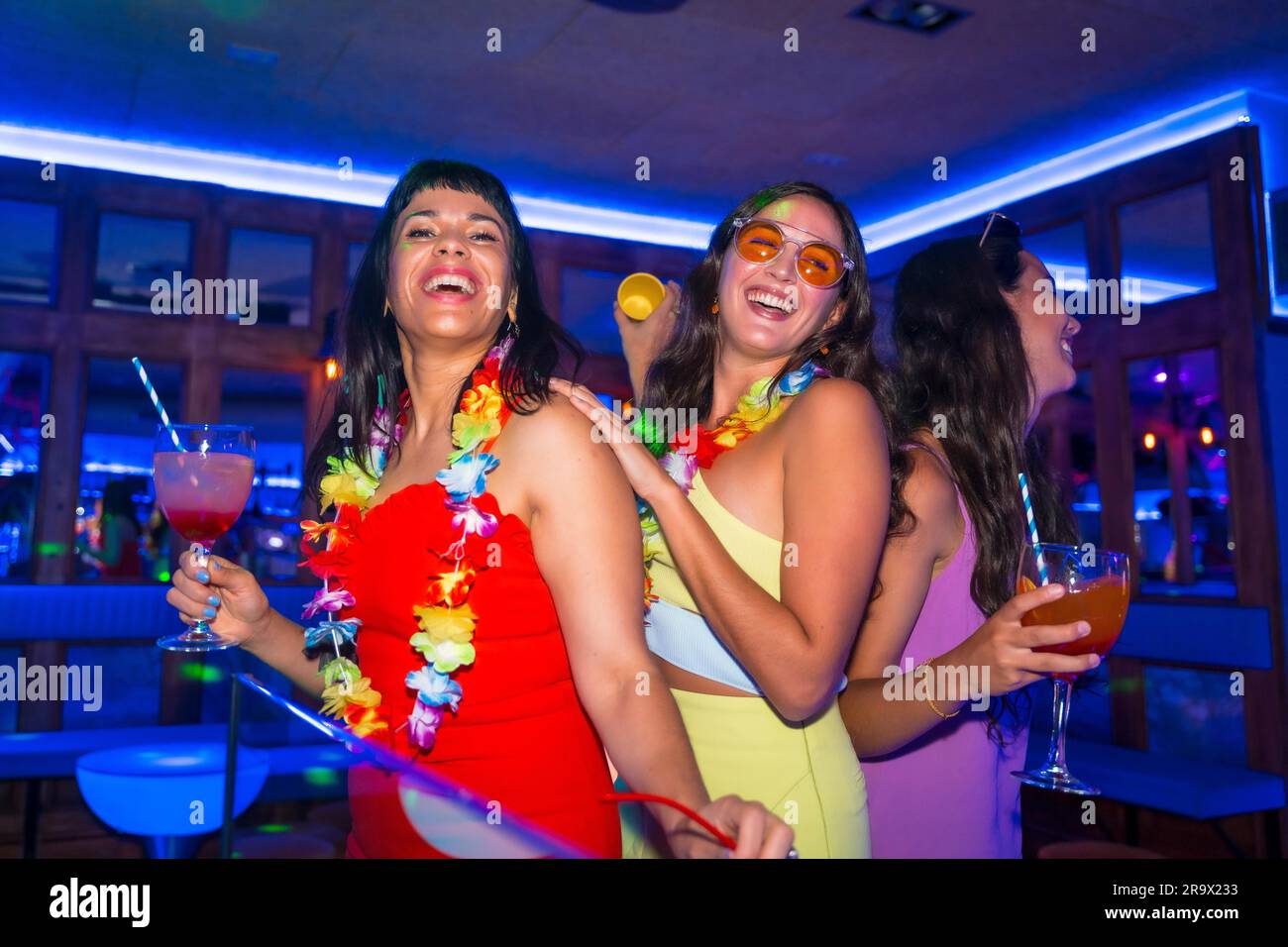Des amies féminines dansent dans une boîte de nuit avec des verres d'alcool souriant lors d'une soirée en vacances d'été Banque D'Images