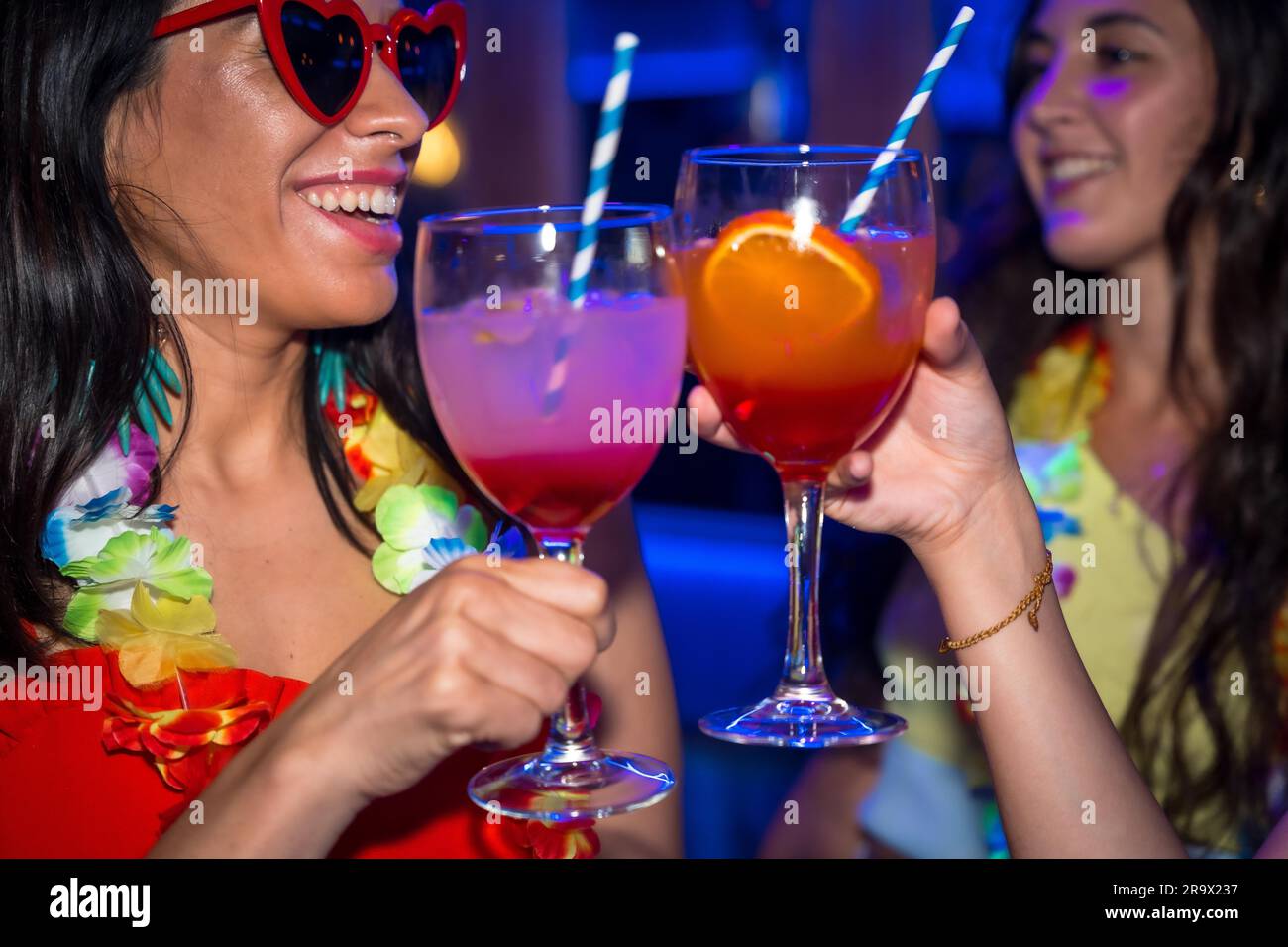 Des amies dans une boîte de nuit en train de craquer avec des verres d'alcool souriant lors d'une soirée Banque D'Images