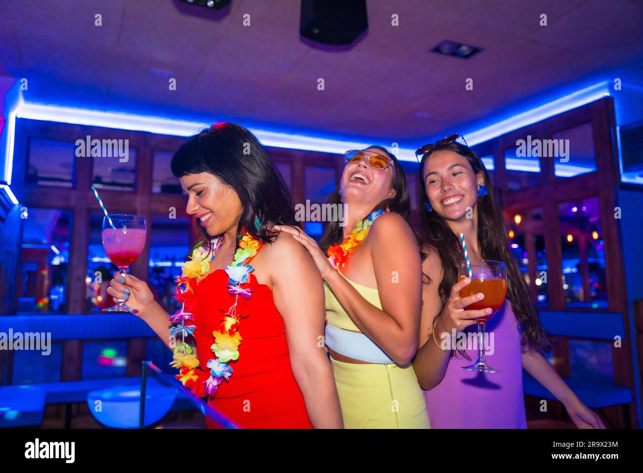 Des amies féminines dansent dans une boîte de nuit avec des verres d'alcool souriant lors d'une soirée en vacances d'été Banque D'Images