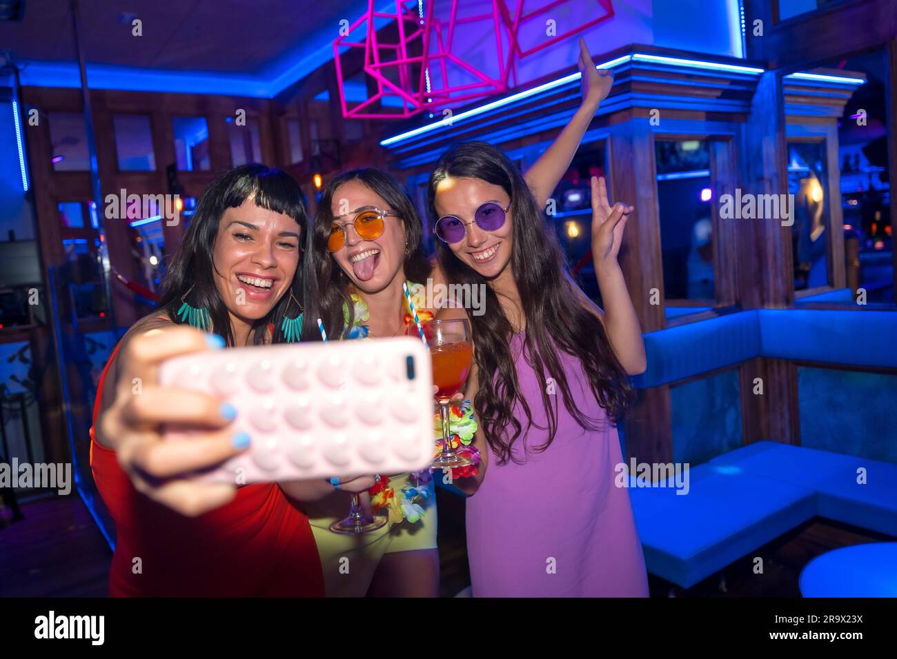 Des amis souriants avec des verres d'alcool dans une boîte de nuit prenant un selfie à une fête de nuit Banque D'Images
