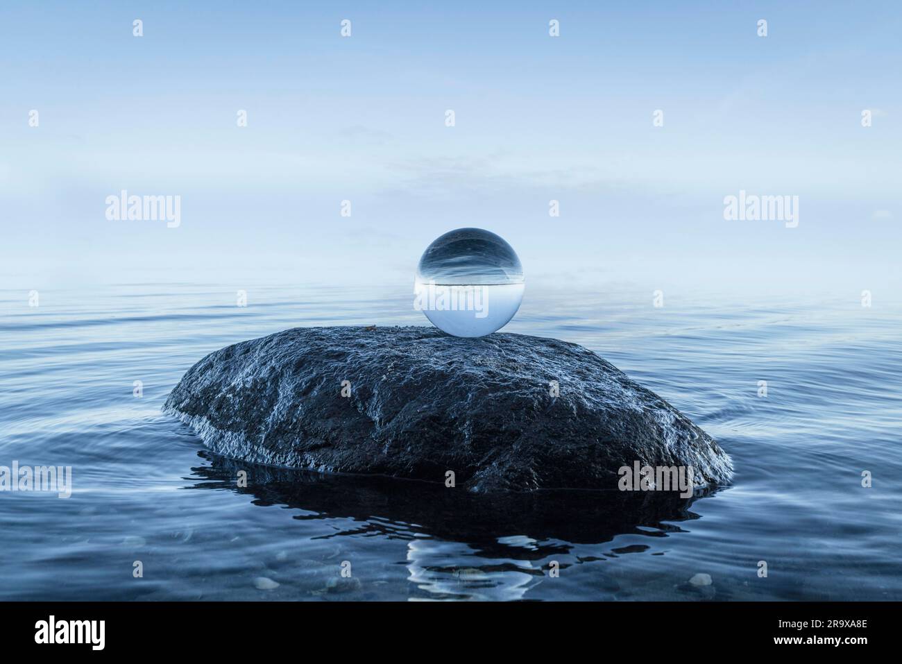 Orbe de cristal sur un grand rocher noir au bord de l'océan bleu un matin silencieux Banque D'Images