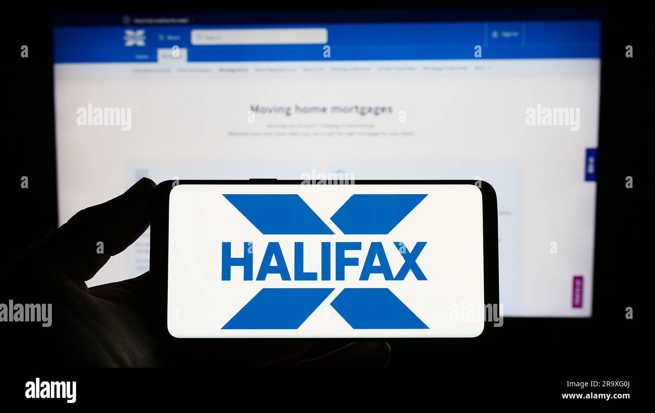 Personne tenant un smartphone avec le logo de la société britannique de services financiers Halifax à l'écran devant le site Web. Mise au point sur l'affichage du téléphone. Banque D'Images