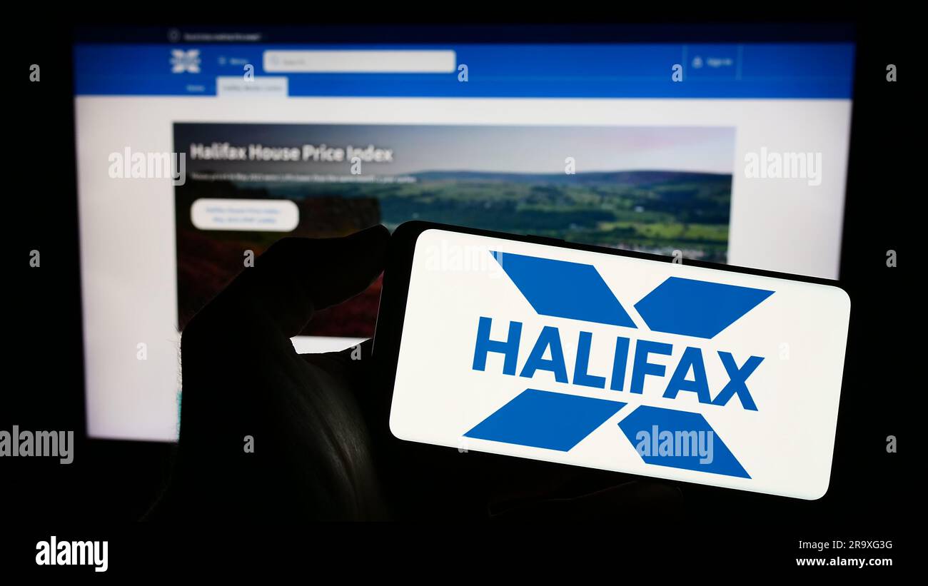 Personne tenant un téléphone cellulaire avec le logo de la société britannique de services financiers Halifax à l'écran devant la page Web des affaires. Mise au point sur l'affichage du téléphone. Banque D'Images