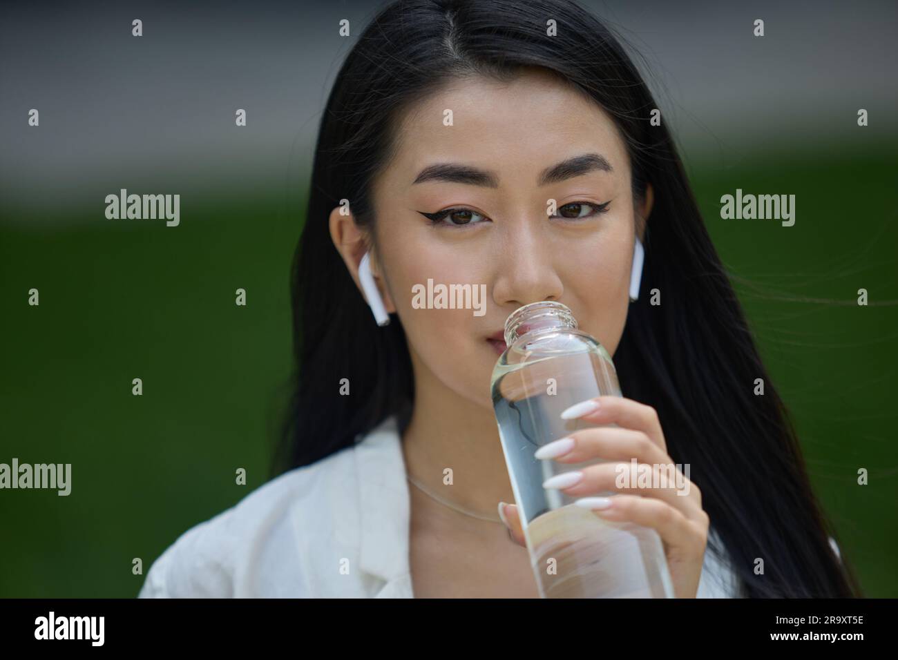 Portrait d'une belle jeune femme vietnamienne qui boit de l'eau. Une femme de démonstration attirante qui écoute de la musique dans un casque sans fil et prend un verre Banque D'Images