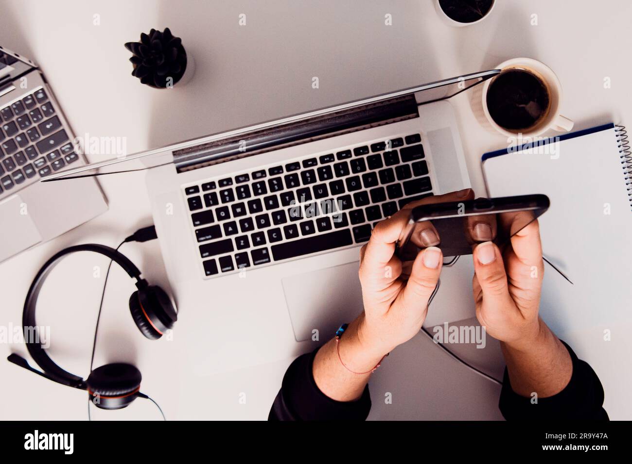Un homme qui utilise un smartphone sur une table à côté d'un ordinateur portable ouvert avec un casque Banque D'Images