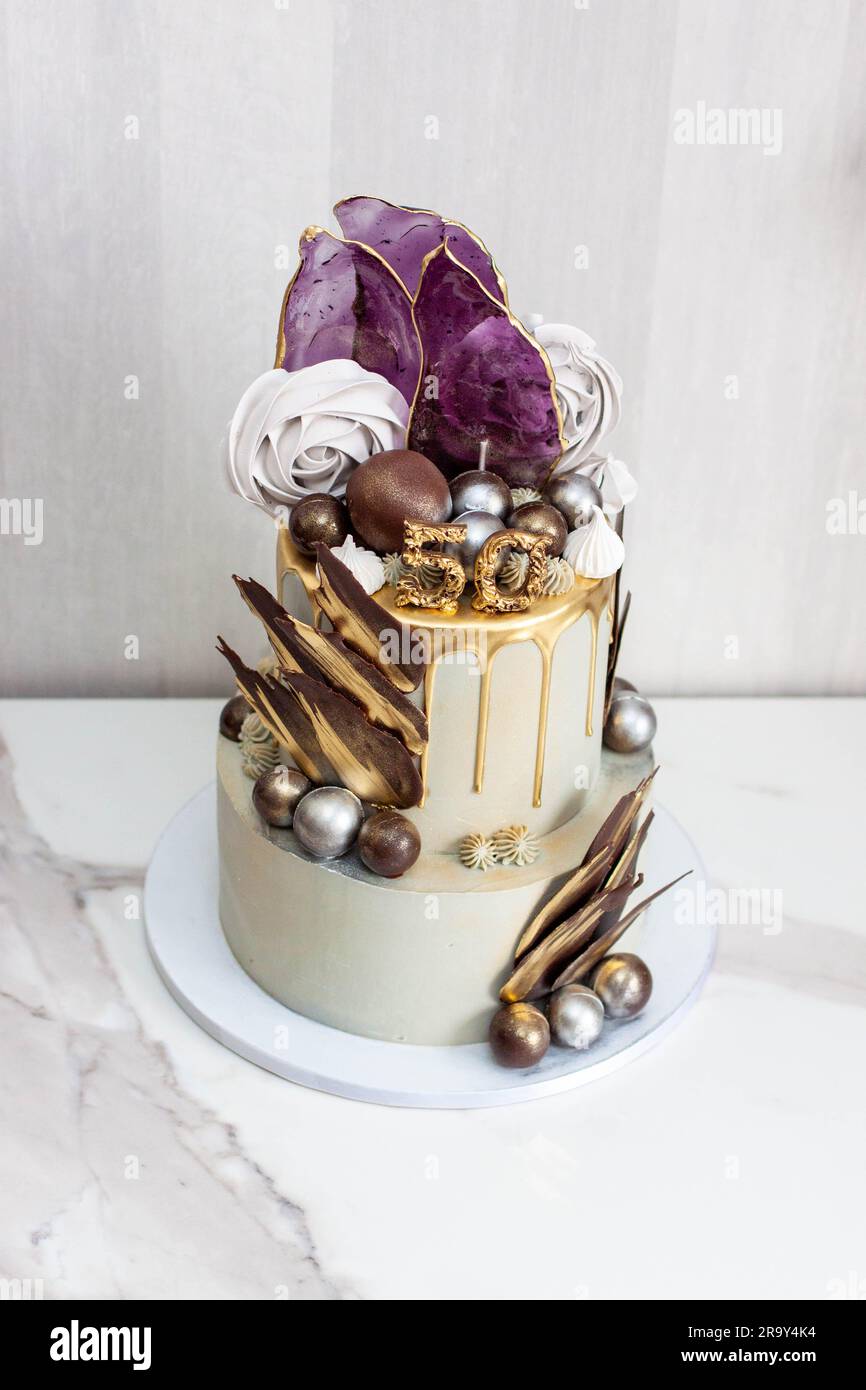 Grand gâteau gris et doré élégant à deux couches pour un anniversaire d'homme, décoré d'isomalt, de meringues, de sphères de chocolat et de pétales Banque D'Images