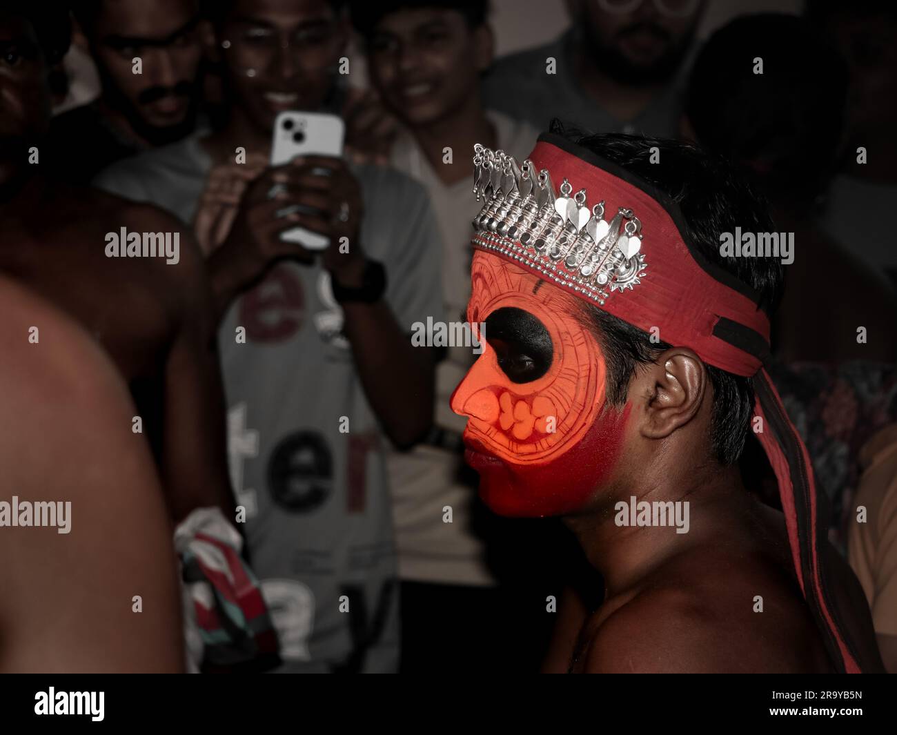 les gens en public prenant des photos d'un artiste theyyam décoré avec de la peinture faciale brillante ad maquillage lors d'un événement religieux traditionnel tenu dans le kerala, ind Banque D'Images