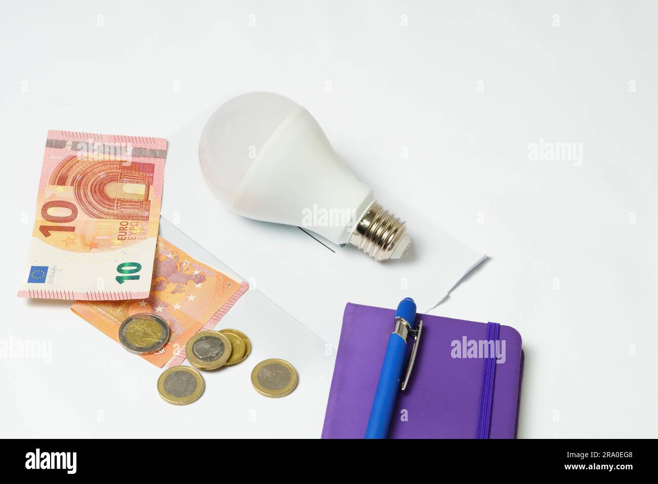 Ampoule sur une facture d'électricité et billets et pièces sur fond blanc. Notion d'augmentation du prix de l'électricité Banque D'Images
