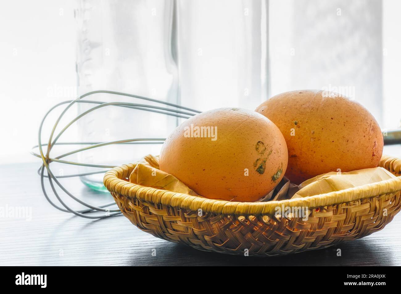 Deux œufs frais juste jeté, dans un petit panier, avec un fouet à spirale Banque D'Images