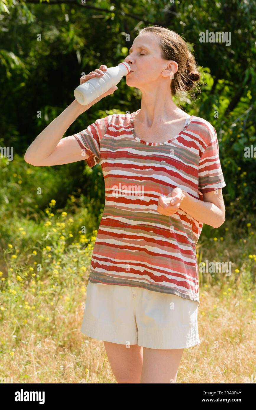Une femme âgée boit de l'eau ou du yogourt pour étancher sa soif après une longue course dans la forêt Banque D'Images