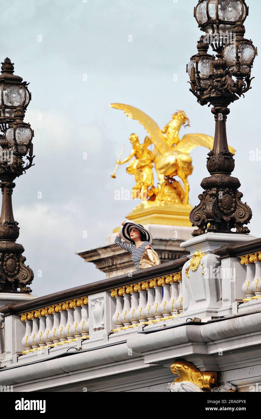 Une femme à la mode à Paris, qui donne sur le pont Alexandre III des Beaux-Arts, entre des lampes Art Nouveau ornées et une sculpture en or Pegasus. Banque D'Images