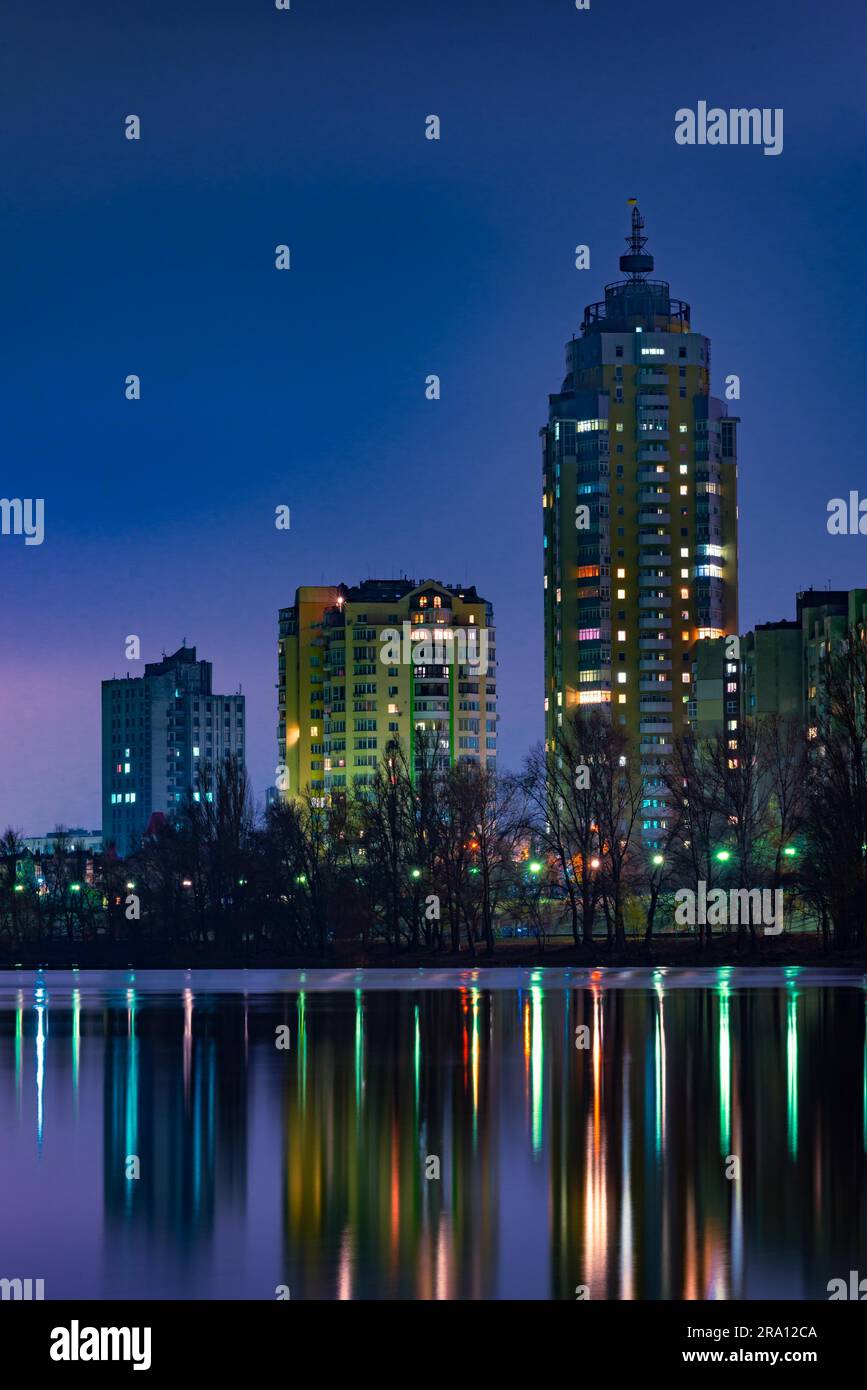 Vue nocturne des bâtiments modernes dans le quartier Obolon de Kiev, Ukraine, près du fleuve Dnieper, les lumières se reflètent sur l'eau calme Banque D'Images