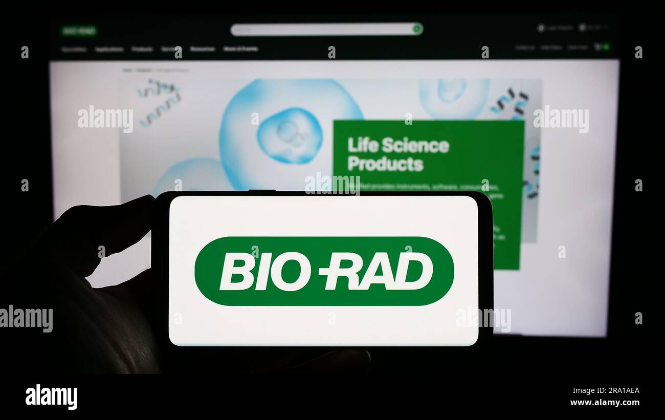 Personne tenant un téléphone portable avec le logo de la société américaine Bio-Rad Laboratories Inc. À l'écran en face de la page Web d'affaires. Mise au point sur l'affichage du téléphone. Banque D'Images