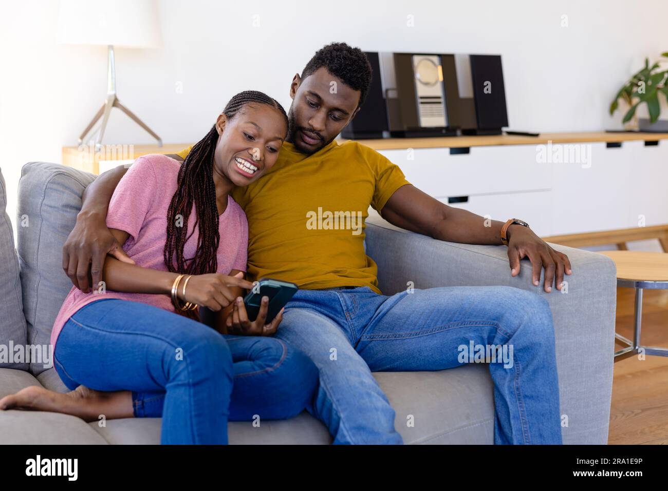 Heureux couple afro-américain utilisant smartphone dans le salon Banque D'Images