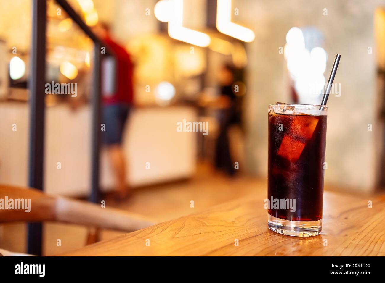 Un verre de délicieux café avec des glaçons et une paille sur fond de bois. Délicieux cocktail froid sur le fond du bar et les gens dans le café ou Banque D'Images