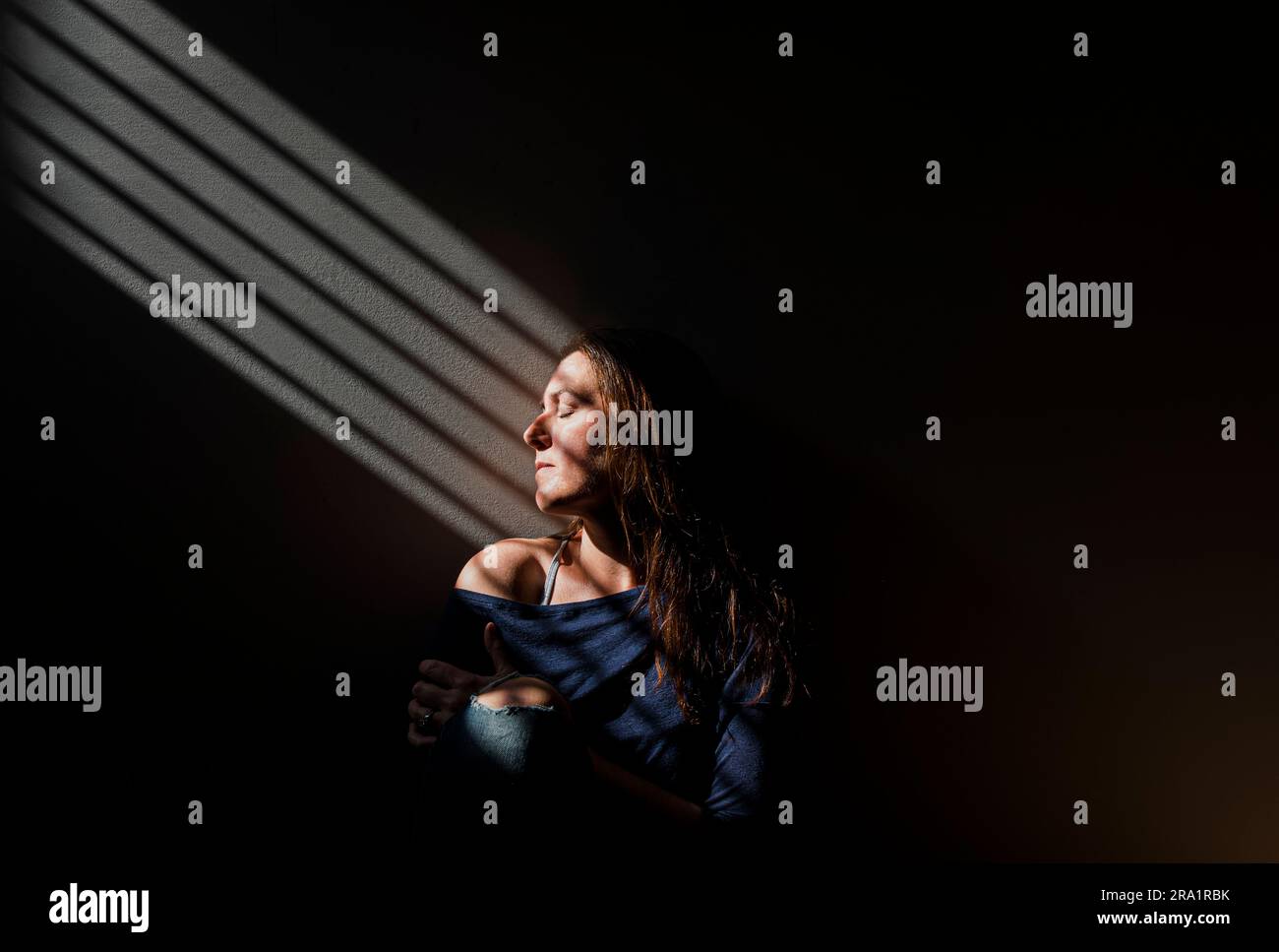 Profil de la femme avec les yeux fermés dans un patch de lumière une pièce sombre. Banque D'Images