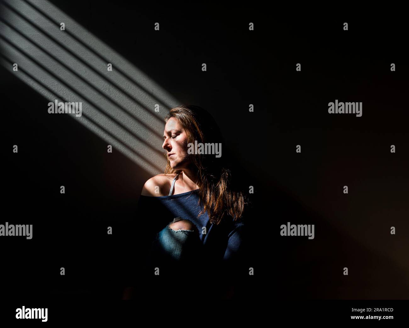 Profil d'une femme assise dans une zone de lumière dans une pièce sombre. Banque D'Images