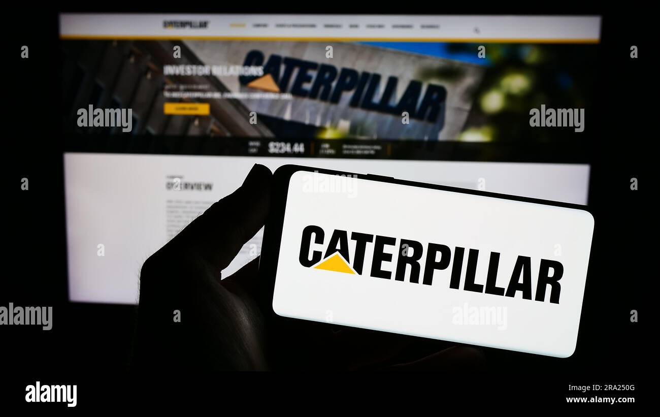 Personne portant un smartphone portant le logo de la société américaine d'équipements lourds Caterpillar Inc. À l'écran, devant le site Web. Mise au point sur l'affichage du téléphone. Banque D'Images