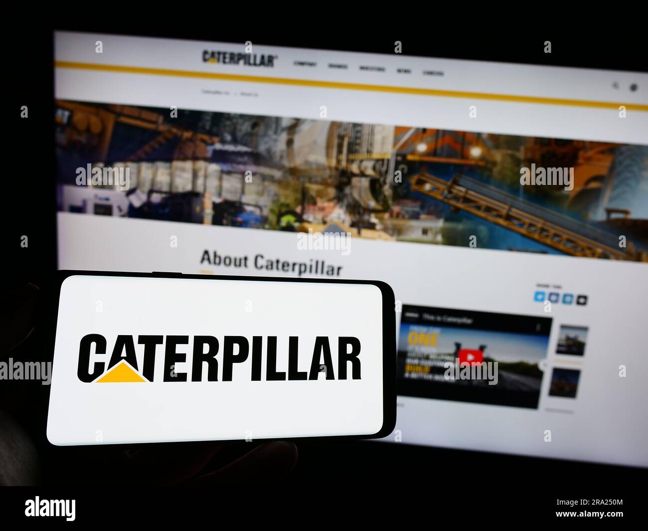 Personne tenant un téléphone portable portant le logo de la société américaine d'équipements lourds Caterpillar Inc. À l'écran, en face de la page Web de l'entreprise. Mise au point sur l'affichage du téléphone. Banque D'Images
