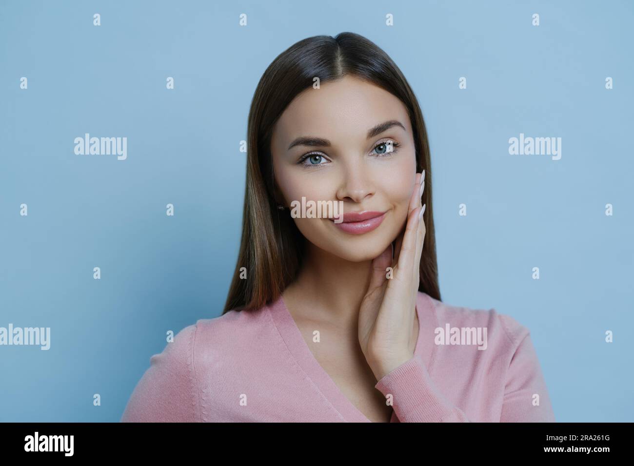 Adorable femme touche joue, aime la peau douce après le masque ou la crème, regarde à la caméra, isolé. Banque D'Images