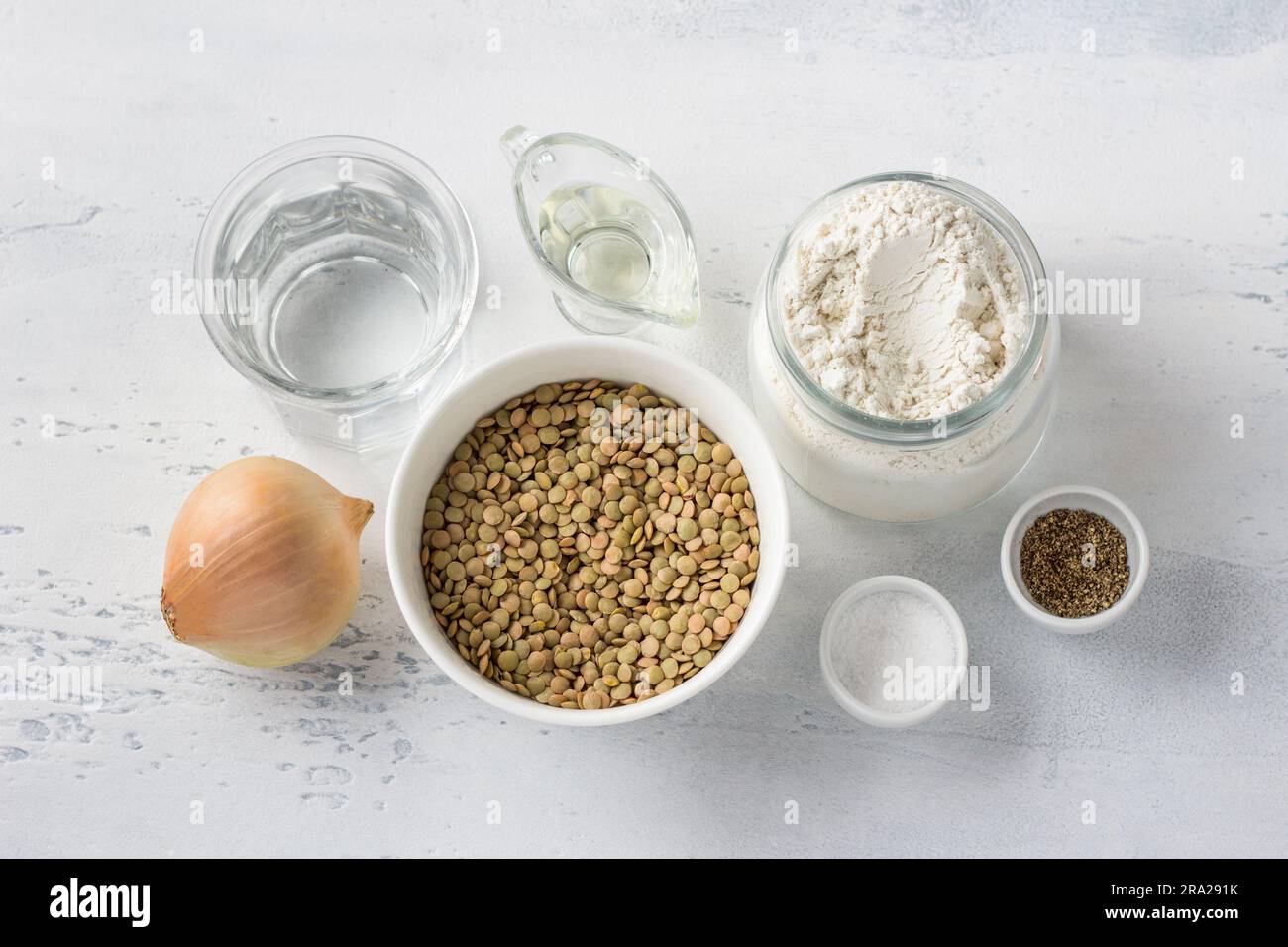 Ingrédients : lentilles vertes, oignons, farine, eau, huile végétale, sel et poivre sur fond bleu clair, vue du dessus. Cuisine délicieuse nourriture végétalienne. Banque D'Images