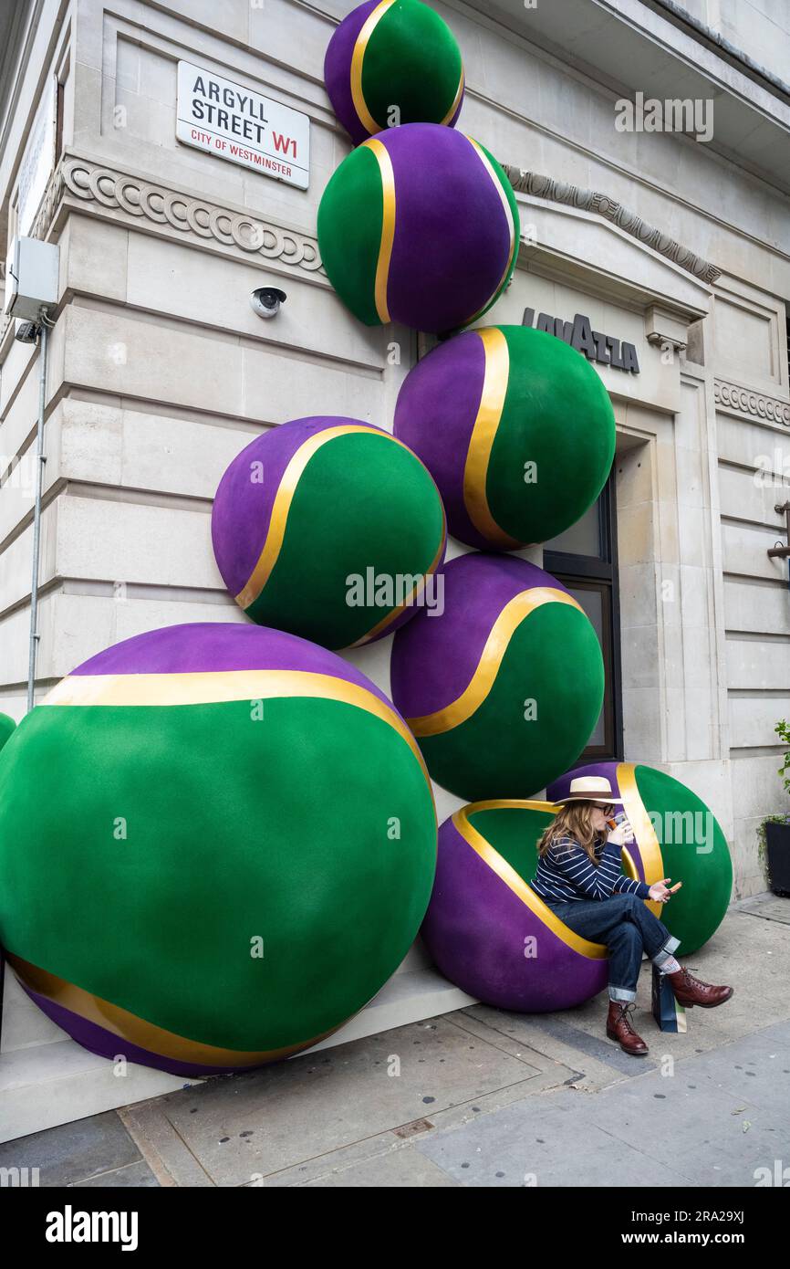 Londres, Royaume-Uni. 30 juin 2023. Une femme s'assoit à boire un café à côté des décorations géantes de balles de tennis inspirées de Wimbledon à l'extérieur du magasin Lavazza sur Argyll Street. Le tournoi annuel de tennis de Wimbledon de deux semaines commence la semaine prochaine. Credit: Stephen Chung / Alamy Live News Banque D'Images
