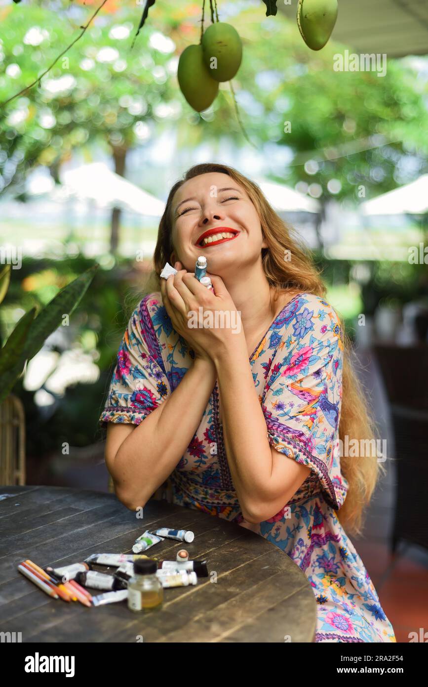 Portrait de belle femme blonde artiste et illustrateur assis à la table et tenant heureusement ses peintures acryliques Banque D'Images