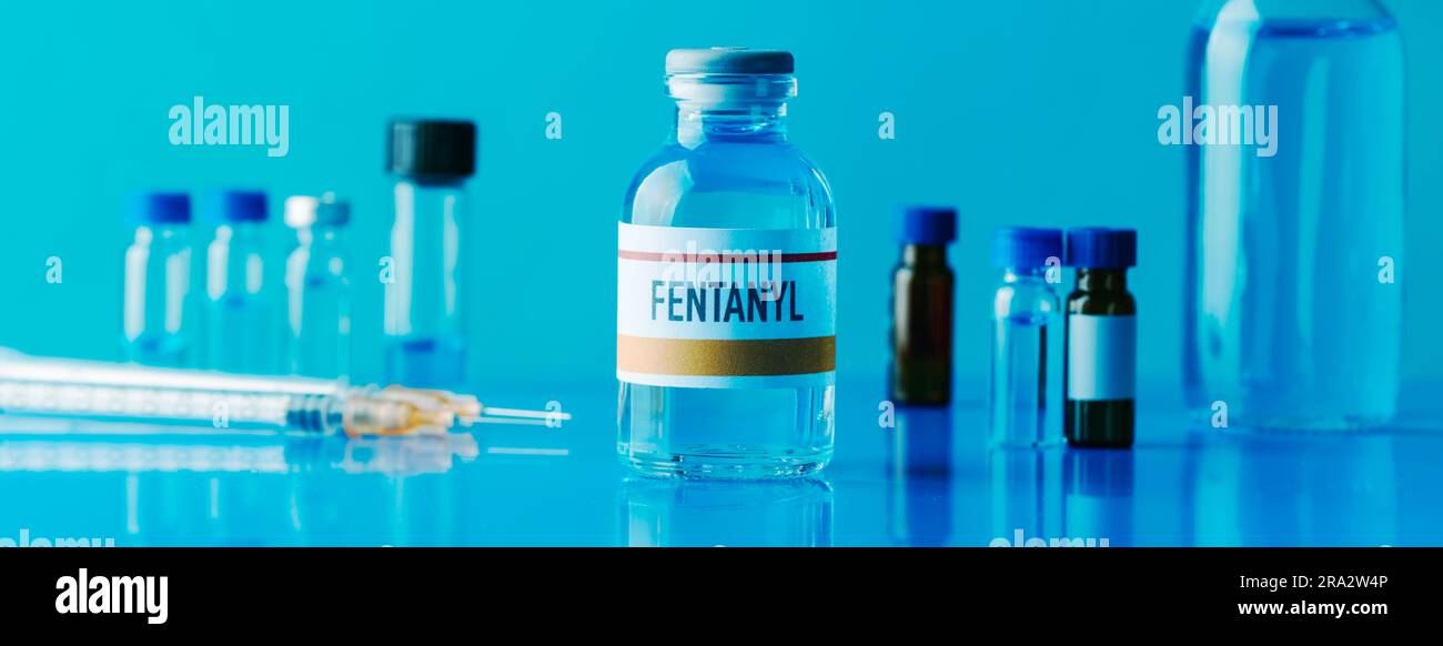 un flacon simulé de fentanyl à côté d'une seringue et d'autres flacons différents sur une table bleue, dans un format panoramique à utiliser comme bannière web Banque D'Images