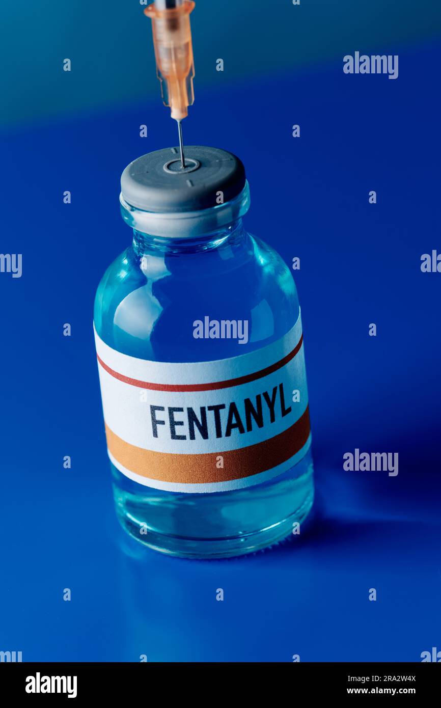 gros plan d'un flacon simulé de fentanyl avec une seringue bloquée dans son bouchon sur une table bleue Banque D'Images