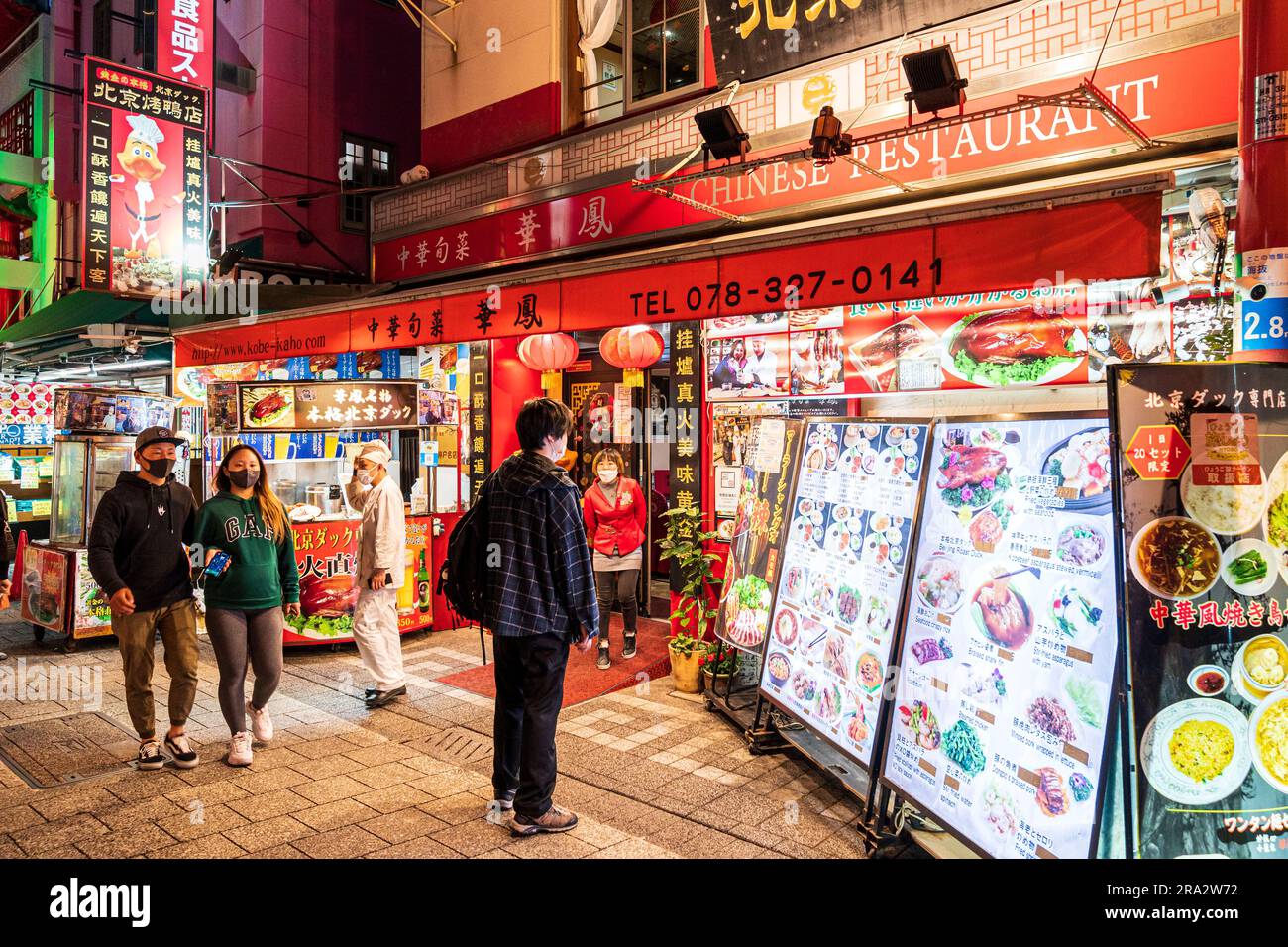 Extérieur d'un restaurant chinois à Chinatown, Kobe, le soir. Accueillir à l'extérieur temping jeune n pour venir à l'intérieur comme il regarde le tableau de menu. Banque D'Images